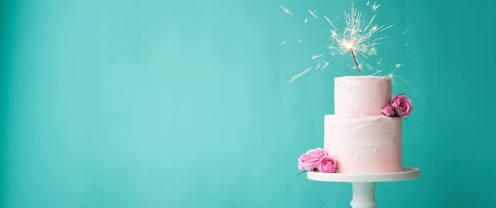 White wedding cake with pink flower garnish against a teal background